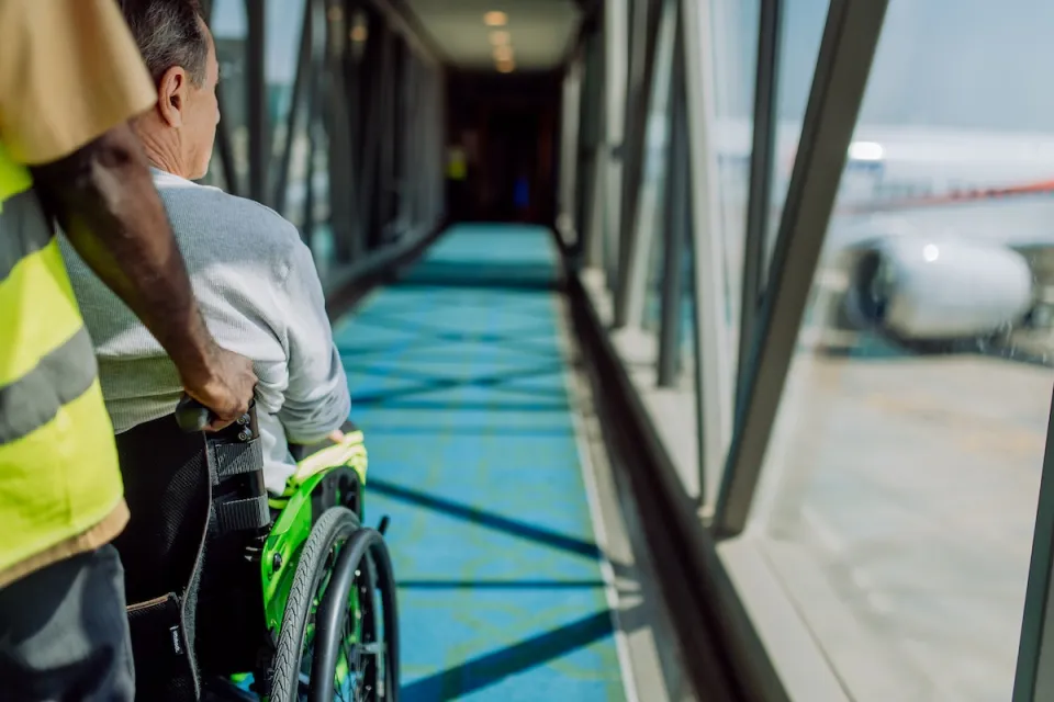 Person pusing person sitting in wheelchair down airplane ramp toward airplane at airport.